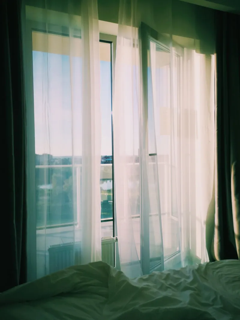 Ventana de balcón abierta con cortinas blancas ventilando una habitación